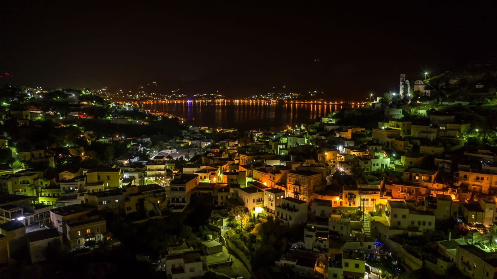 Night panoramic view of the town of Leros with city lights reflecting on the water.